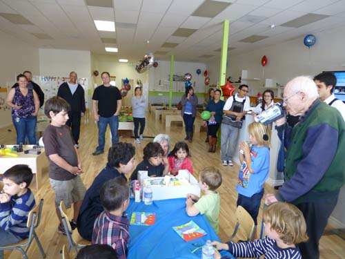 Sky Masori blows the candles on his birthday cake as he watched by his older brother Shor, grandma Nancy and cousin Sara. In foreground great-grandpa Sam videos the occasion bringing together kindergarten classmates and their parents.