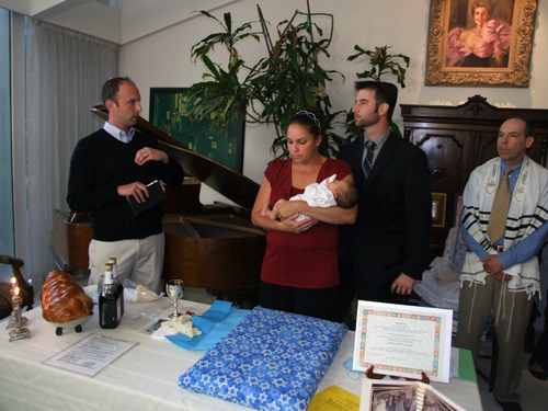 Rabbi Matthew Earne, left, speaks to Samantha and Daniel Greene during naming of baby Jaxson Asher Greene. At right, mohel Dr. Stuart Rubenstein listens