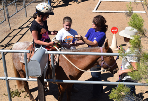 Alise Yamamoto is shown a blue ribbon she earned for the day's lesson on horseback by volunteer Stacey King (in purple) who is flanked by volunteers Bea Weigant and Nancy Edwards