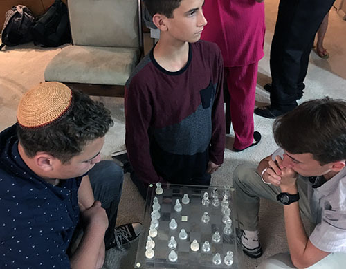 Kyle Taylor, left, plays chess on Erev Shabbat with Yonatan Likhovski as Kyle’s younger brother, Nick, looks away momentarily from kibbitzing.
