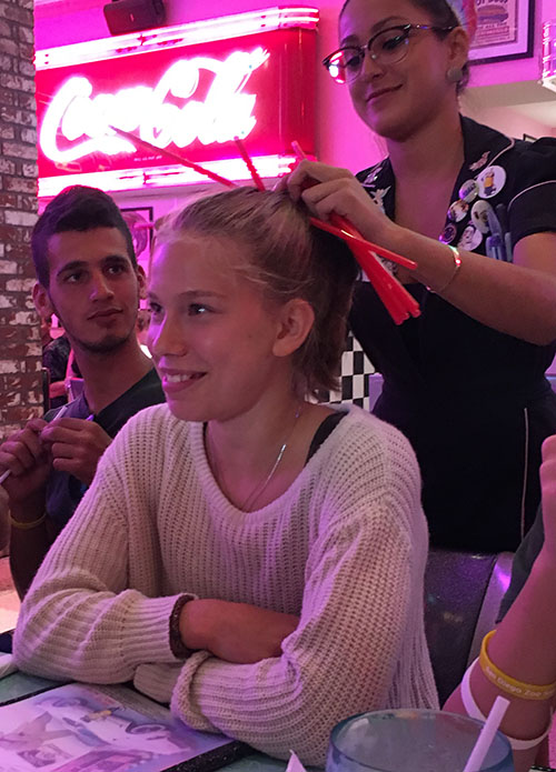 Sophie Taubman is getting her hair done using Corvette’s famous straw bow.